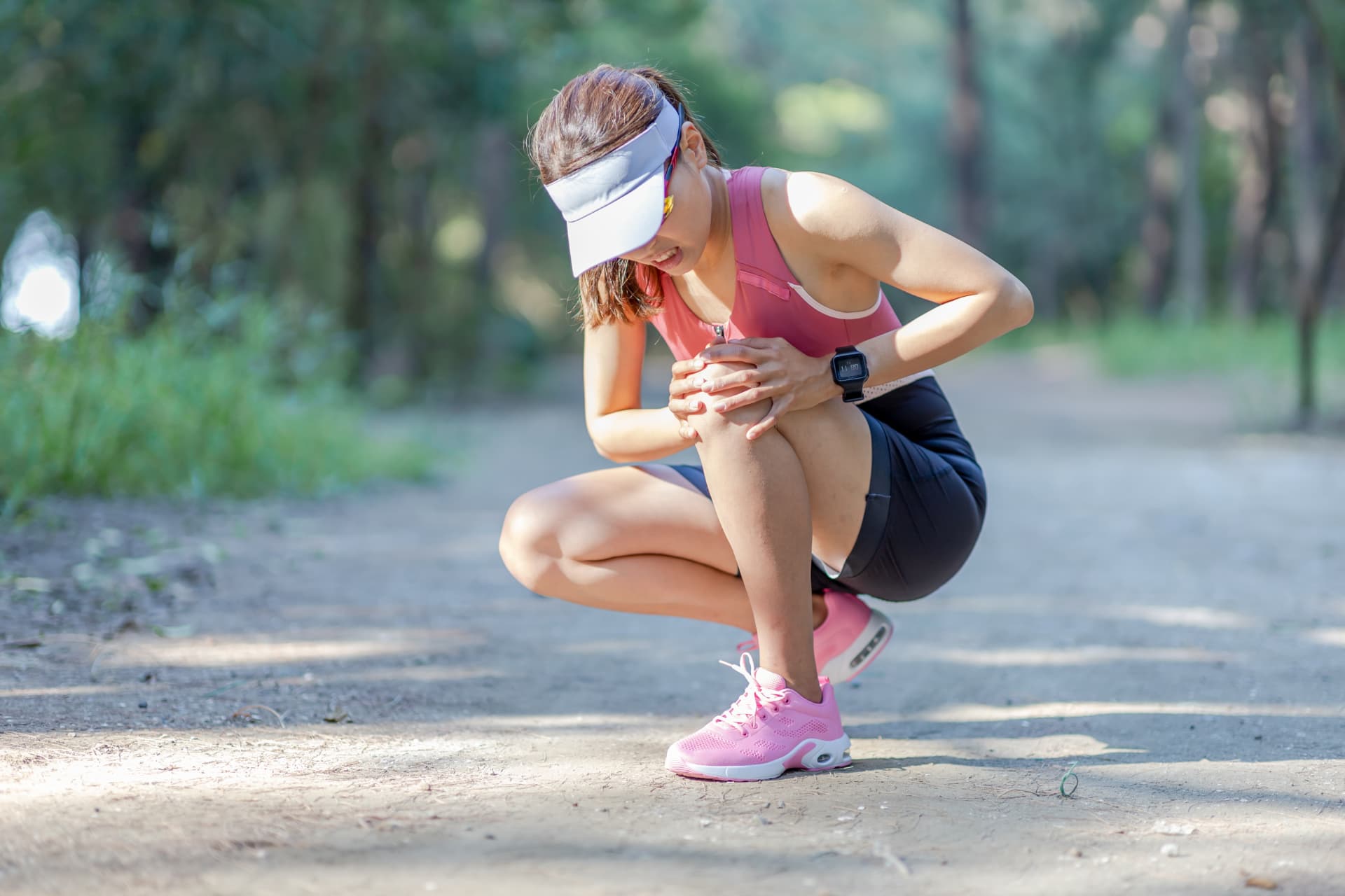 Runner crouched on a trail gripping her painful knee